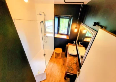 Salle de bain moderne avec douche à l’italienne, vue depuis la fenêtre, et lavabo en bois dans la chambre de Marius à La Maison Folia