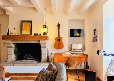 Coin détente du salon de La Maison Folia avec cheminée, guitare et bureau en Normandie