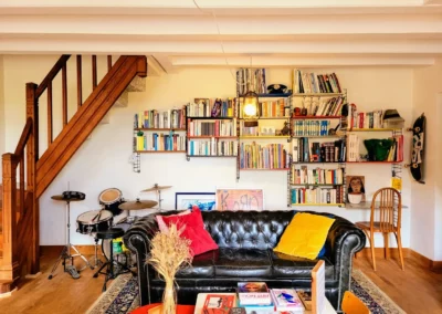 Salon de La Maison Folia avec canapé en cuir, bibliothèque et instruments de musique en Normandie