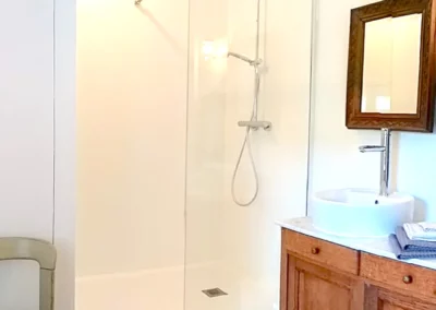 Salle de bain lumineuse avec douche à l’italienne, lavabo et miroir en bois à La Maison Folia.